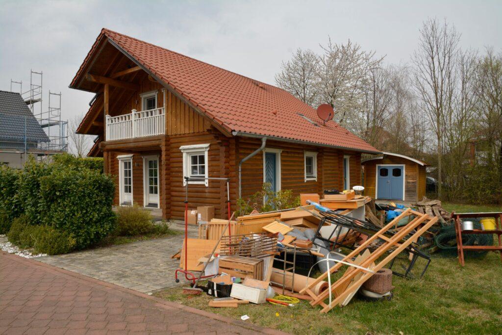 Ein Einfamilienhaus aus Holz mit rotem Ziegeldach, vor dem im Garten diverse Gegenstände und Möbelstücke für eine Entrümpelung aufgestapelt wurden. Das Bild zeigt den Beginn einer Entrümpelung in Mönchengladbach.