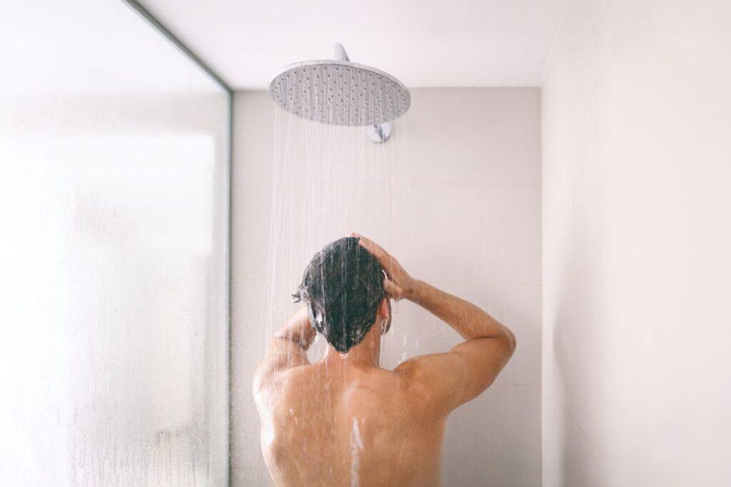 Mann genießt warmes Wasser unter einer Regendusche vor modernen Duschrückwand Platten