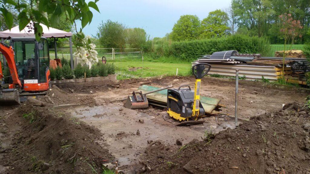 Minibagger Schaufel und Rüttelplatte auf vorbereiteter Gartenfläche für Fundament- oder Terrassenbau