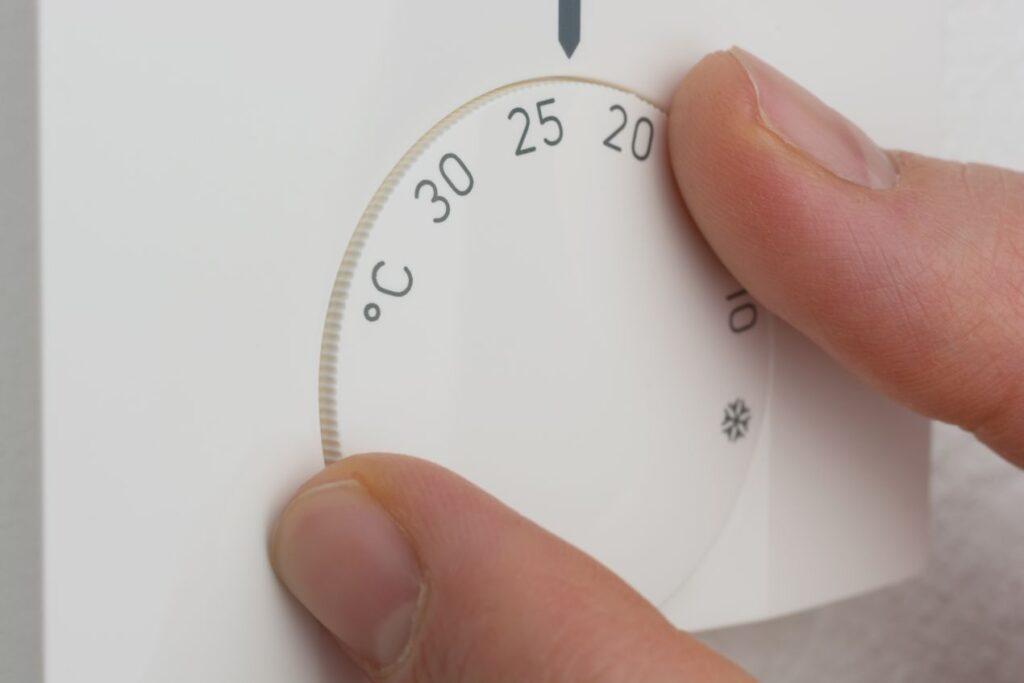 Hand stellt Thermostat auf 22 Grad ein, um Energie zu sparen und die Wirkung einer Fussbodenheizung fraesen optimal zu nutzen